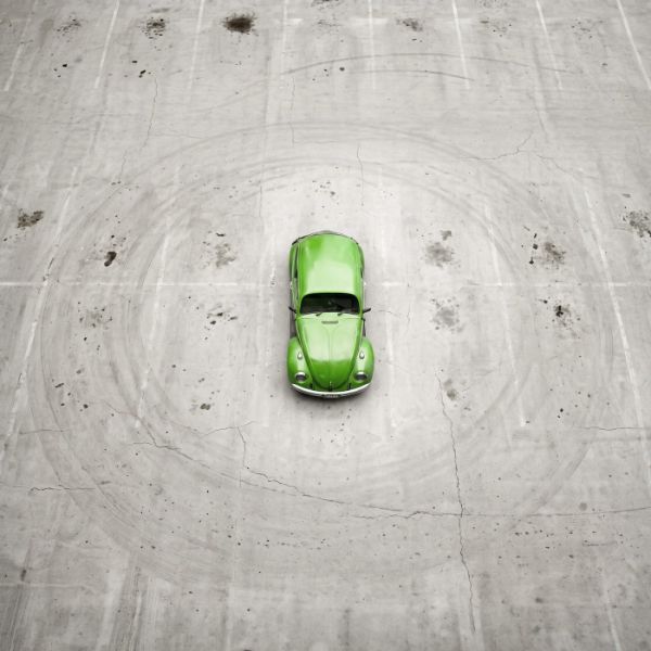 Un Maggiolino verde visto dall'alto, solo al centro di un parcheggio di cemento vuoto